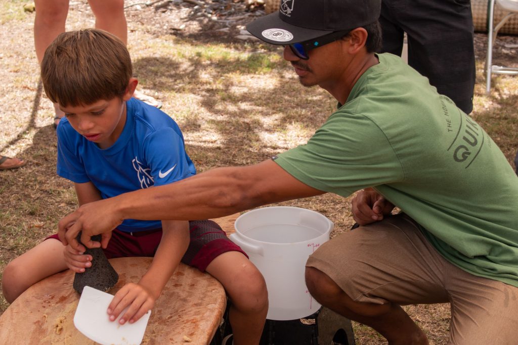 A young man teaching a young boy kuʻi ʻai